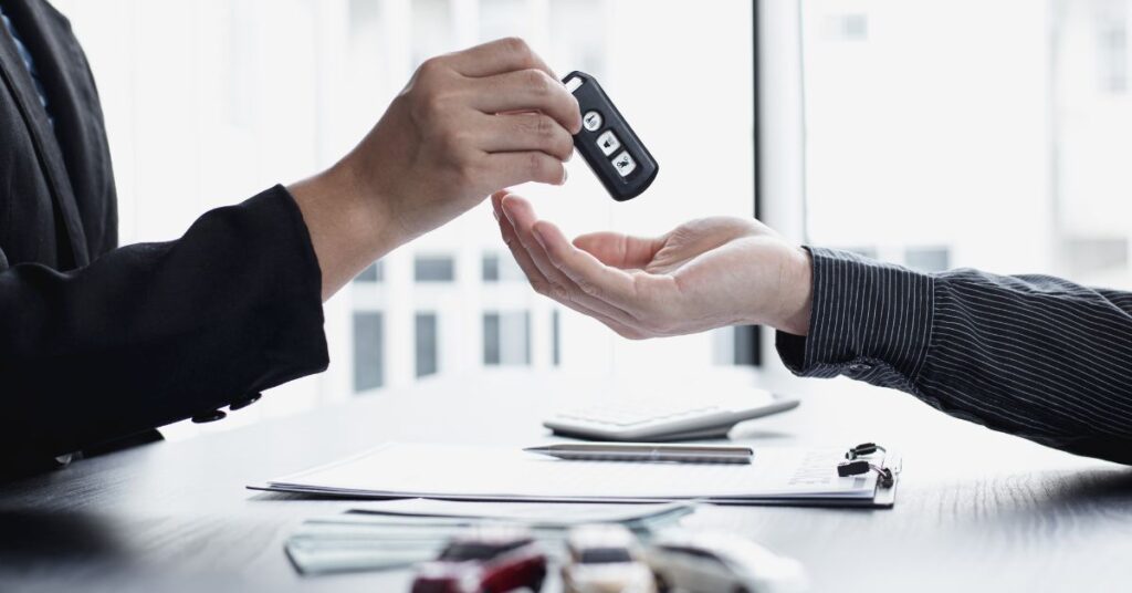 Car salesperson gives the key of a car to the new owner after signing the papers.