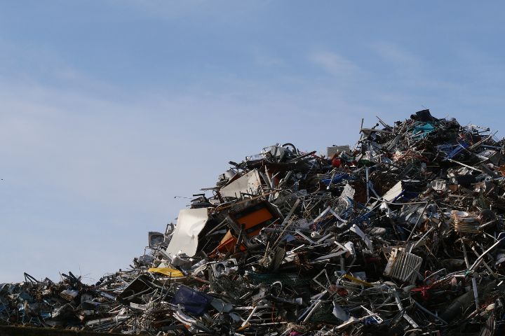 A large heap of twisted metal scraps and debris rises under a clear blue sky in a junkyard.